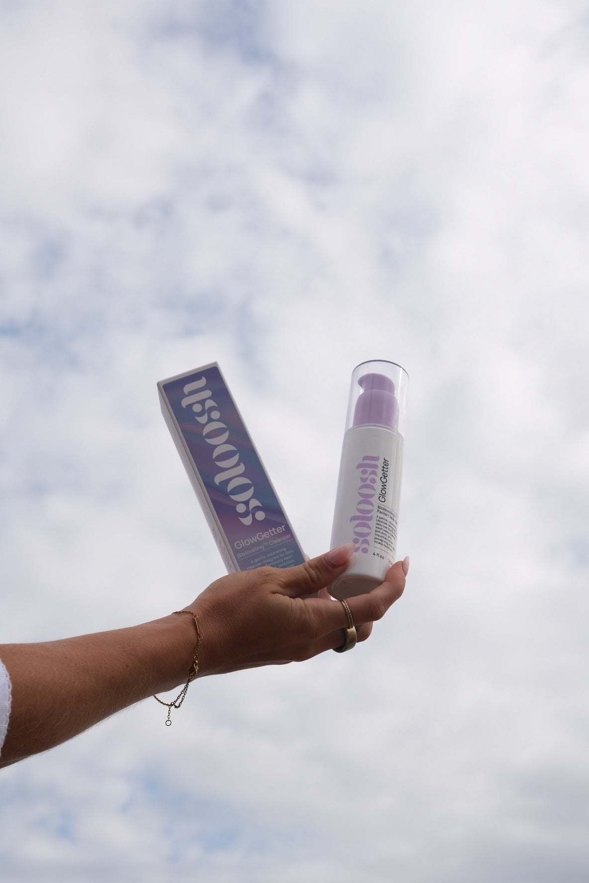 Hand holding a tube and a bottle of cleanser against a cloudy sky